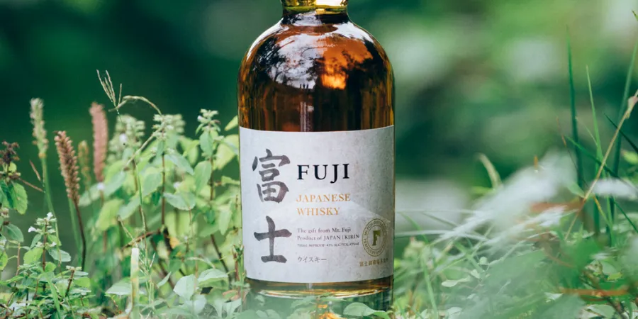 Fuji Japanese Whisky bottle displayed among green plants in an outdoor setting