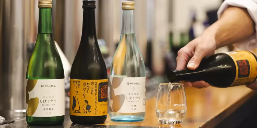 Houraisen Japanese sake being poured into a glass beside three sake bottles on a bar counter