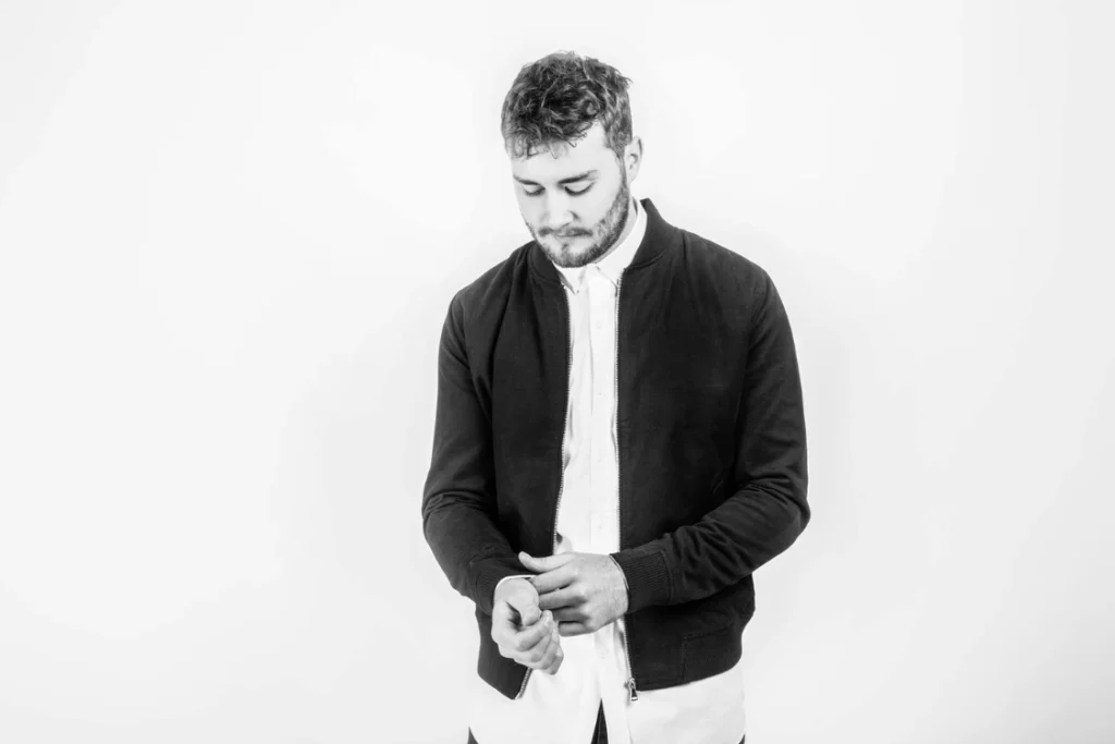 Sam Wills, London-based soul singer, songwriter and producer, pictured in a black-and-white portrait wearing a dark jacket.