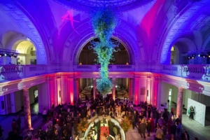 Asian Art in London event in a grand historic venue with vibrant purple lighting, a dramatic glass art installation and guests gathered for an evening reception