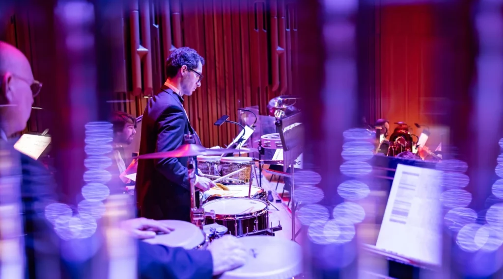 Percussionist performing with the orchestra during The Sound of Epic Anime concert, illuminated by purple and red stage lighting.