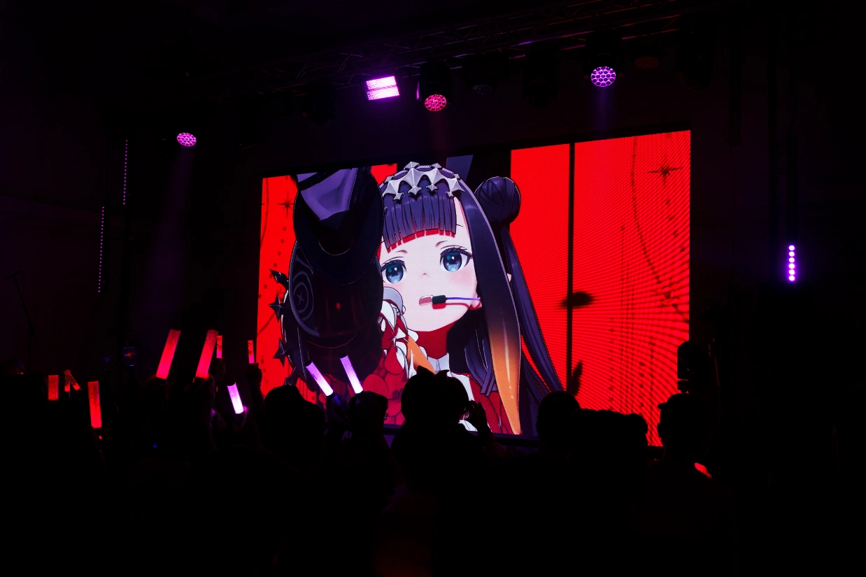 hololive VTuber avatar shown large on a red stage screen, with the audience in silhouette in front of it