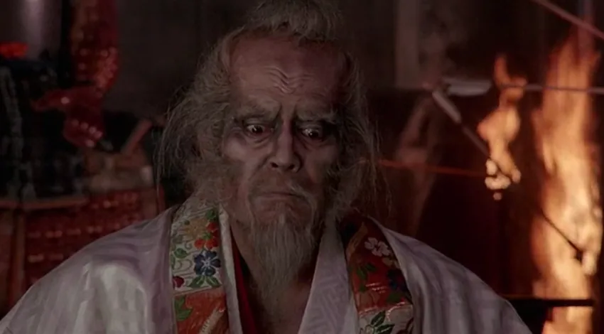 Tatsuya Nakadai in aged makeup as the warlord Hidetora in Akira Kurosawa's Ran, with fire burning behind him.