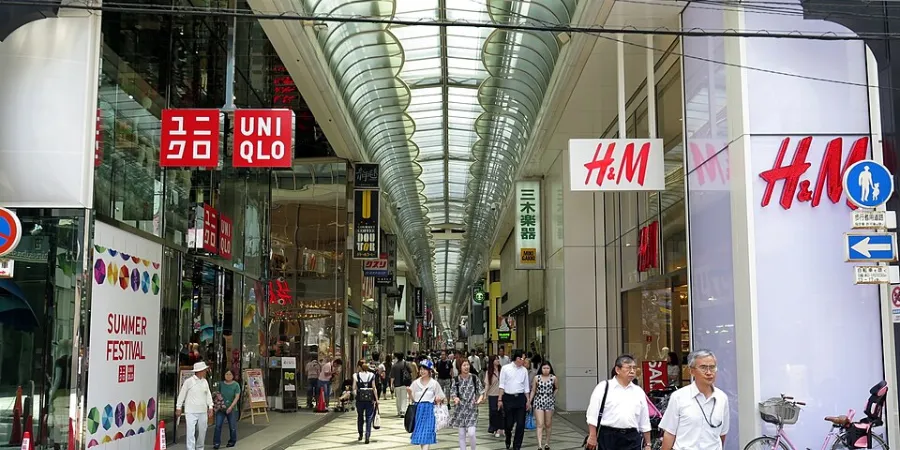 Busy Shinsaibashi shopping arcade in Osaka, Japan, with pedestrians walking beneath a covered glass roof and storefronts including UNIQLO and H&M.