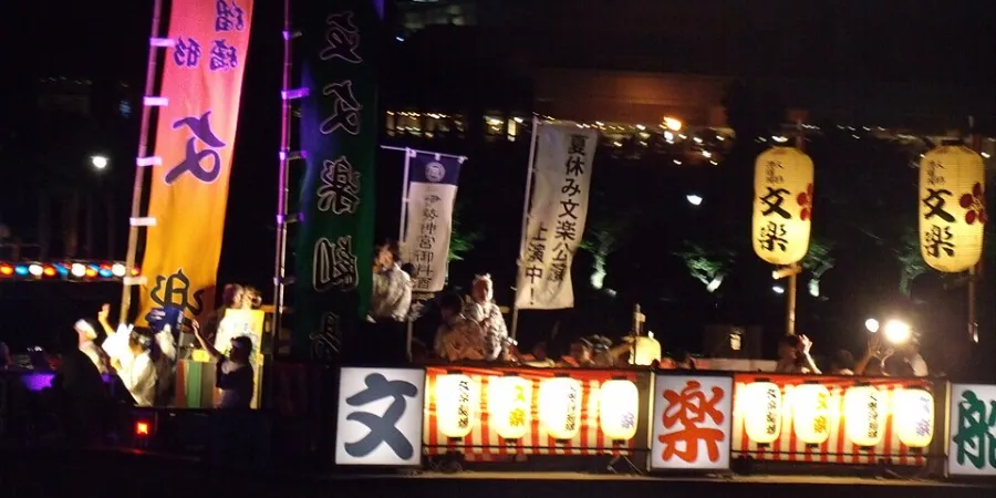 Tenjin Matsuri festival procession in Osaka at night, with illuminated lanterns, traditional Japanese banners, and performers