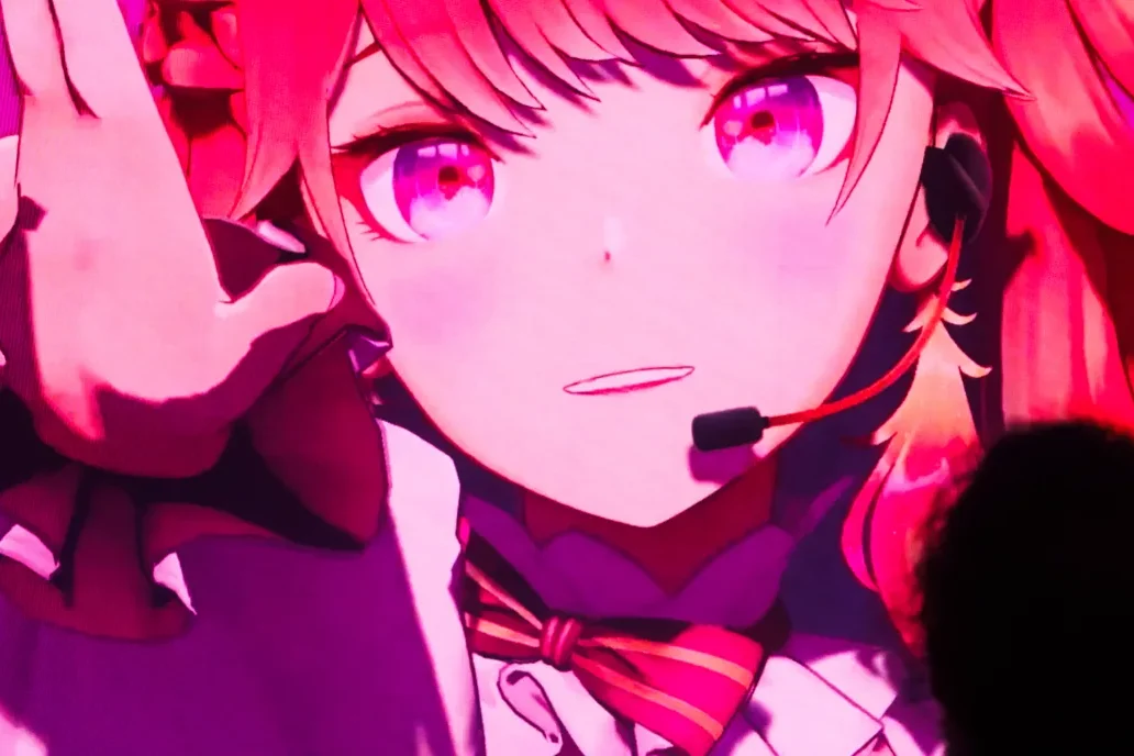 hololive VTuber avatar wearing a headset, shown large and singing on a screen at a London event