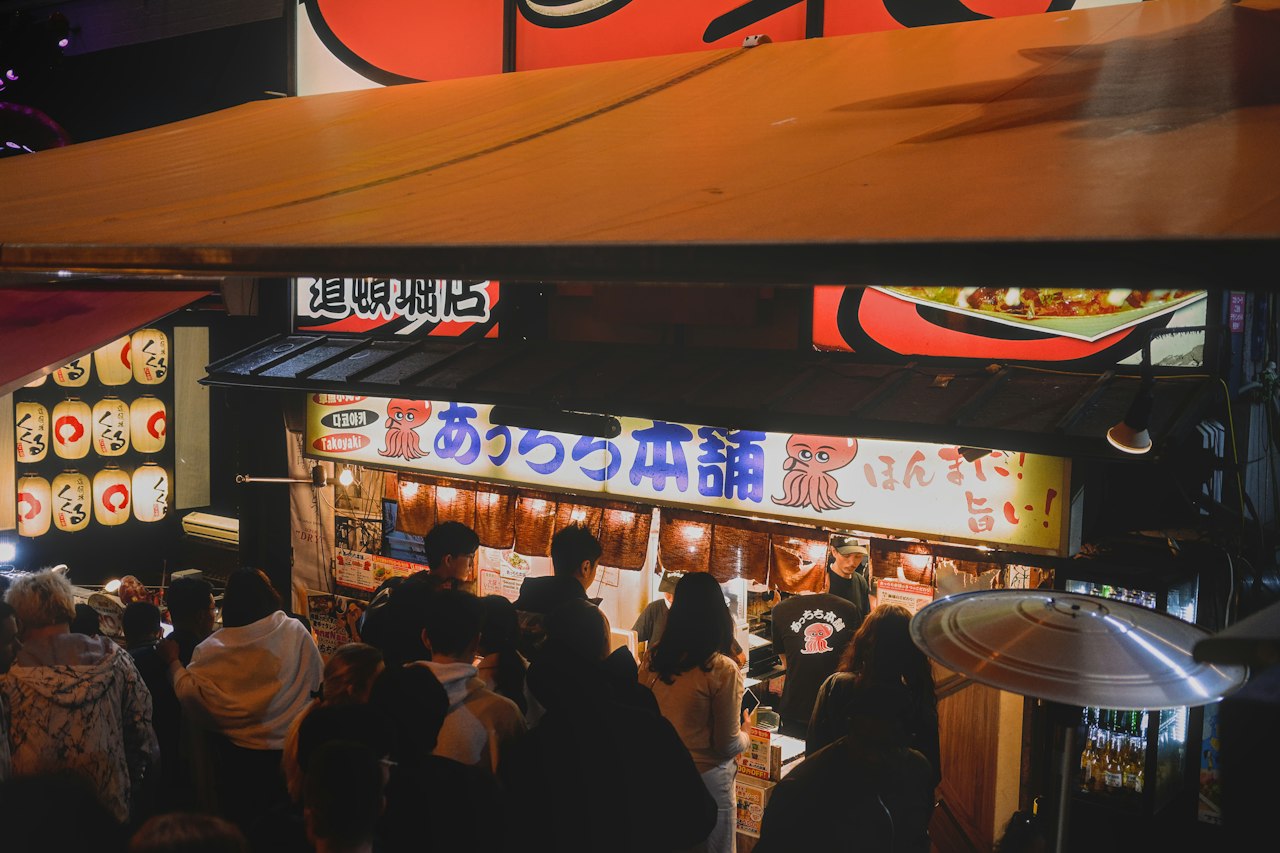 A crowd queuing at the Acchichi Honpo takoyaki stand in Dotonbori, Osaka, at night