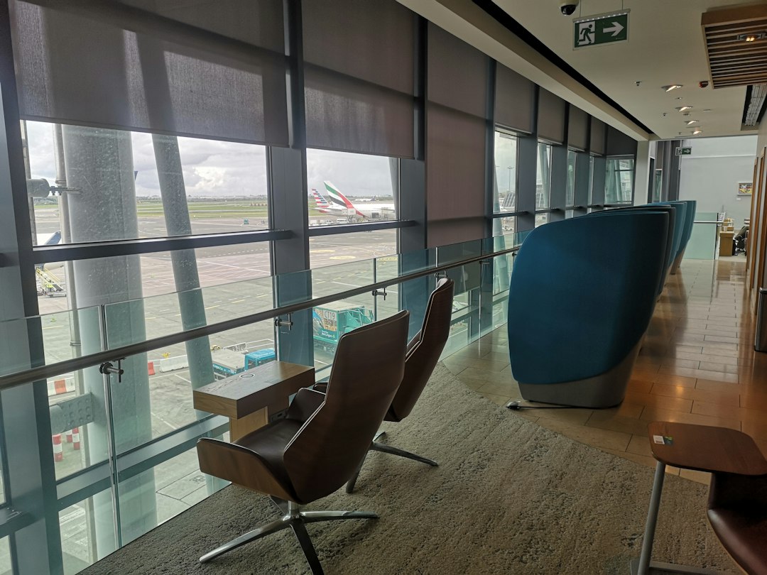 Armchairs and a high-backed seat in an airport lounge beside windows overlooking parked aircraft