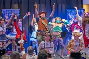 Cosplayers dancing on stage at AnimeCon, in costumes including Attack on Titan Survey Corps uniforms and a Breath of the Wild Gerudo outfit