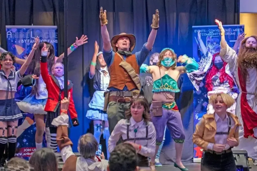 Cosplayers dancing on stage at AnimeCon, in costumes including Attack on Titan Survey Corps uniforms and a Breath of the Wild Gerudo outfit