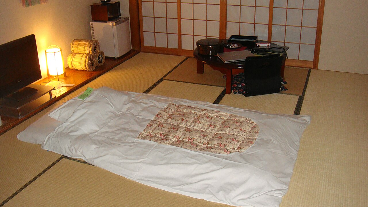 Futon laid out on the tatami floor of a ryokan room with a low table, shoji screens and a paper lamp