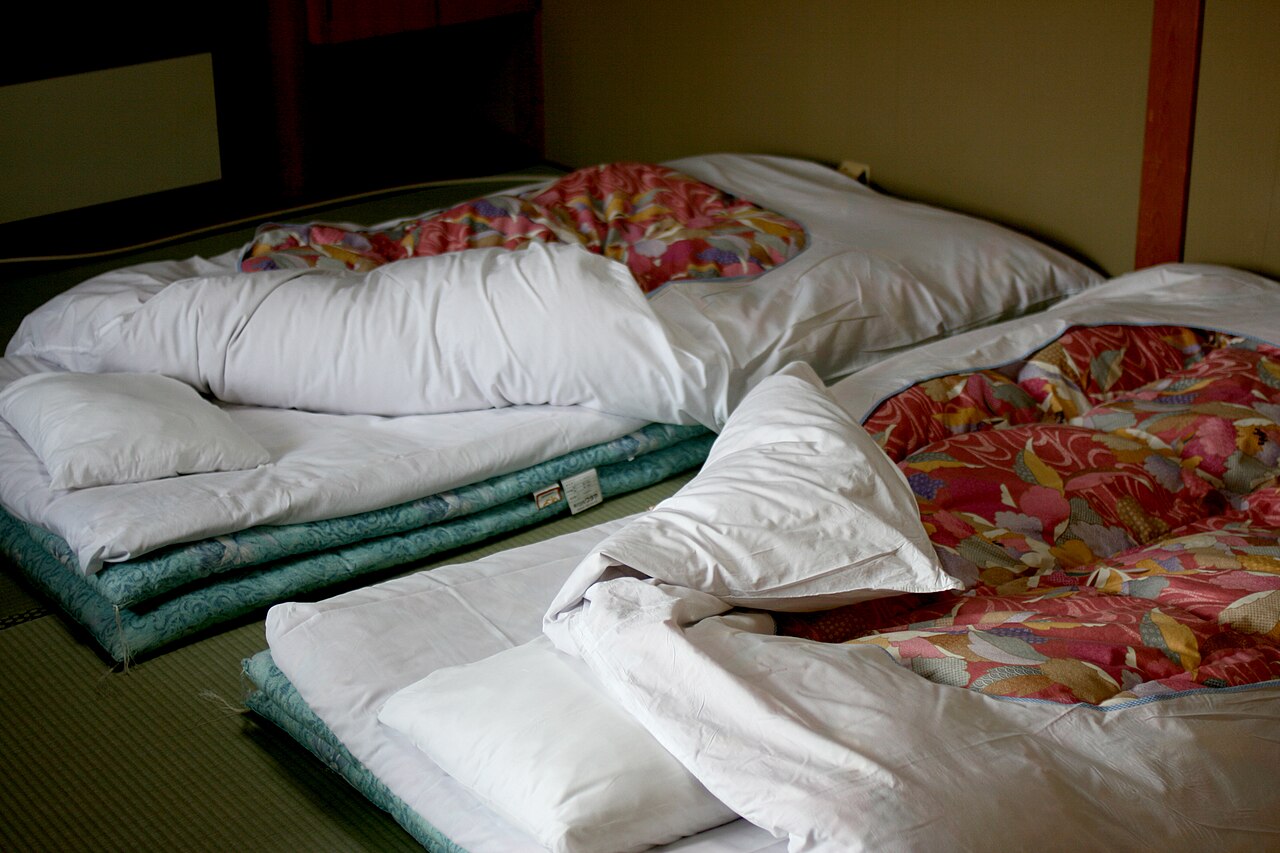 Futons with floral quilts laid out side by side on the tatami floor of a ryokan room at night