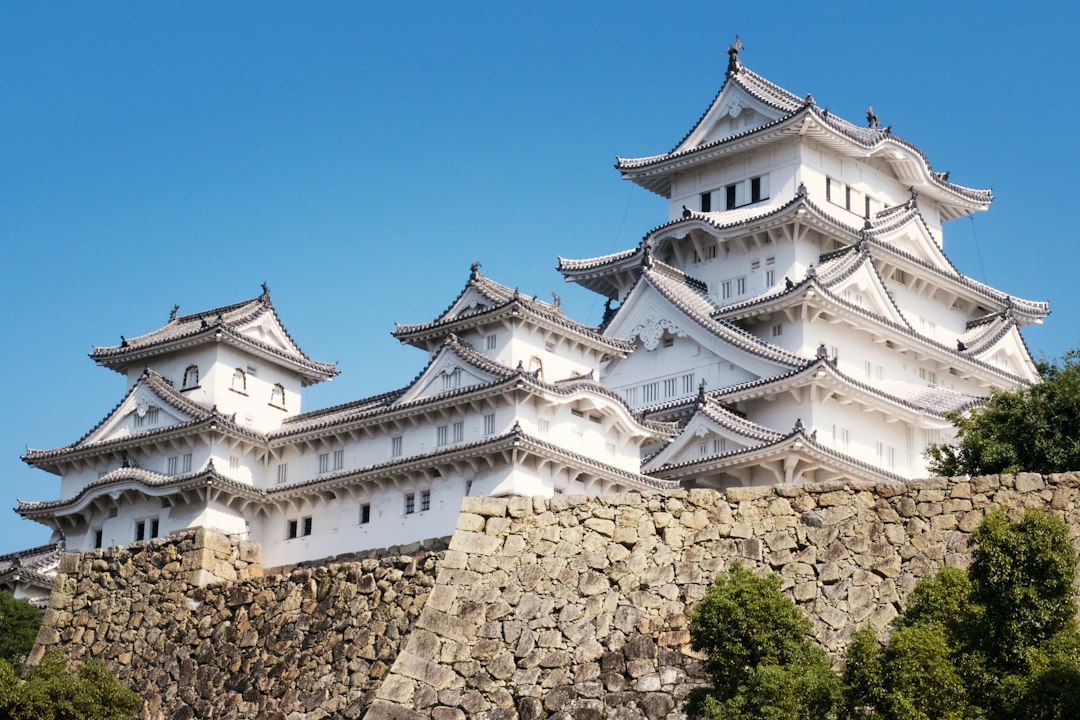 The white multi-tiered keep of Himeji Castle rising above its stone walls under a clear blue sky
