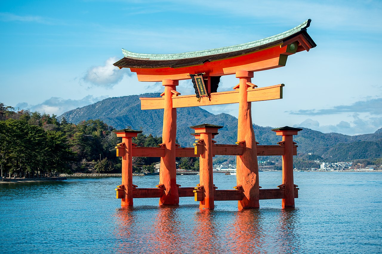 The vermilion Great Torii of Itsukushima Shrine standing in the sea at high tide, with the wooded hills of Miyajima behind