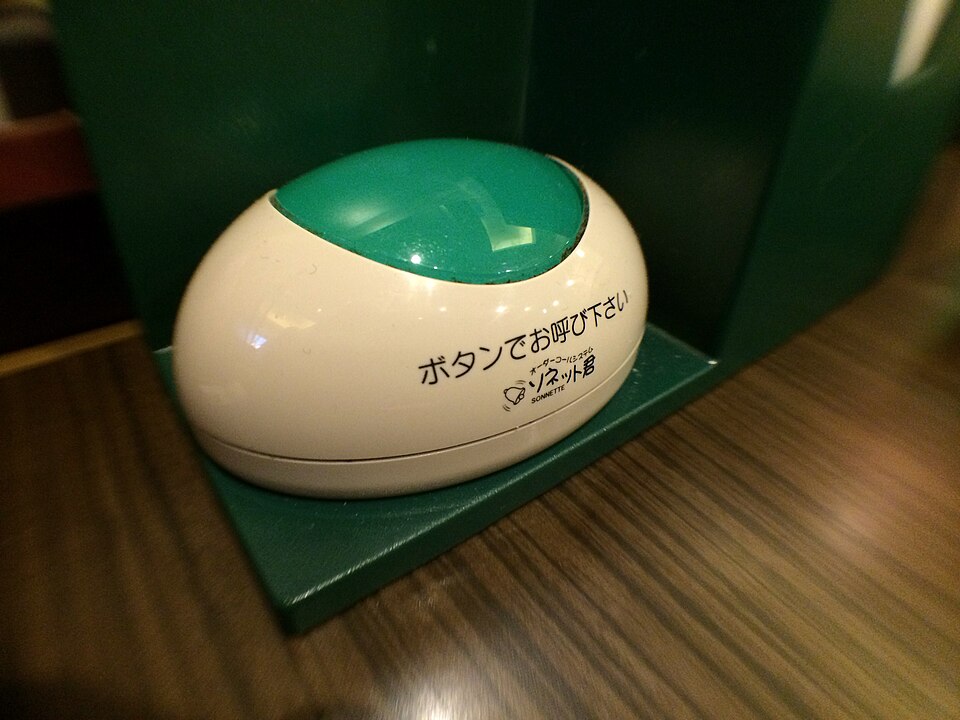 A staff call button on a Japanese restaurant table, labelled in Japanese asking diners to press it to call staff