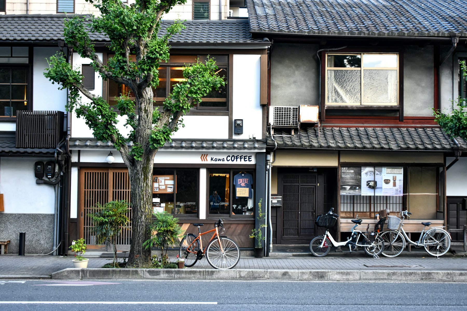 Traditional wooden townhouses and a small coffee shop with bicycles parked outside on a quiet Japanese street