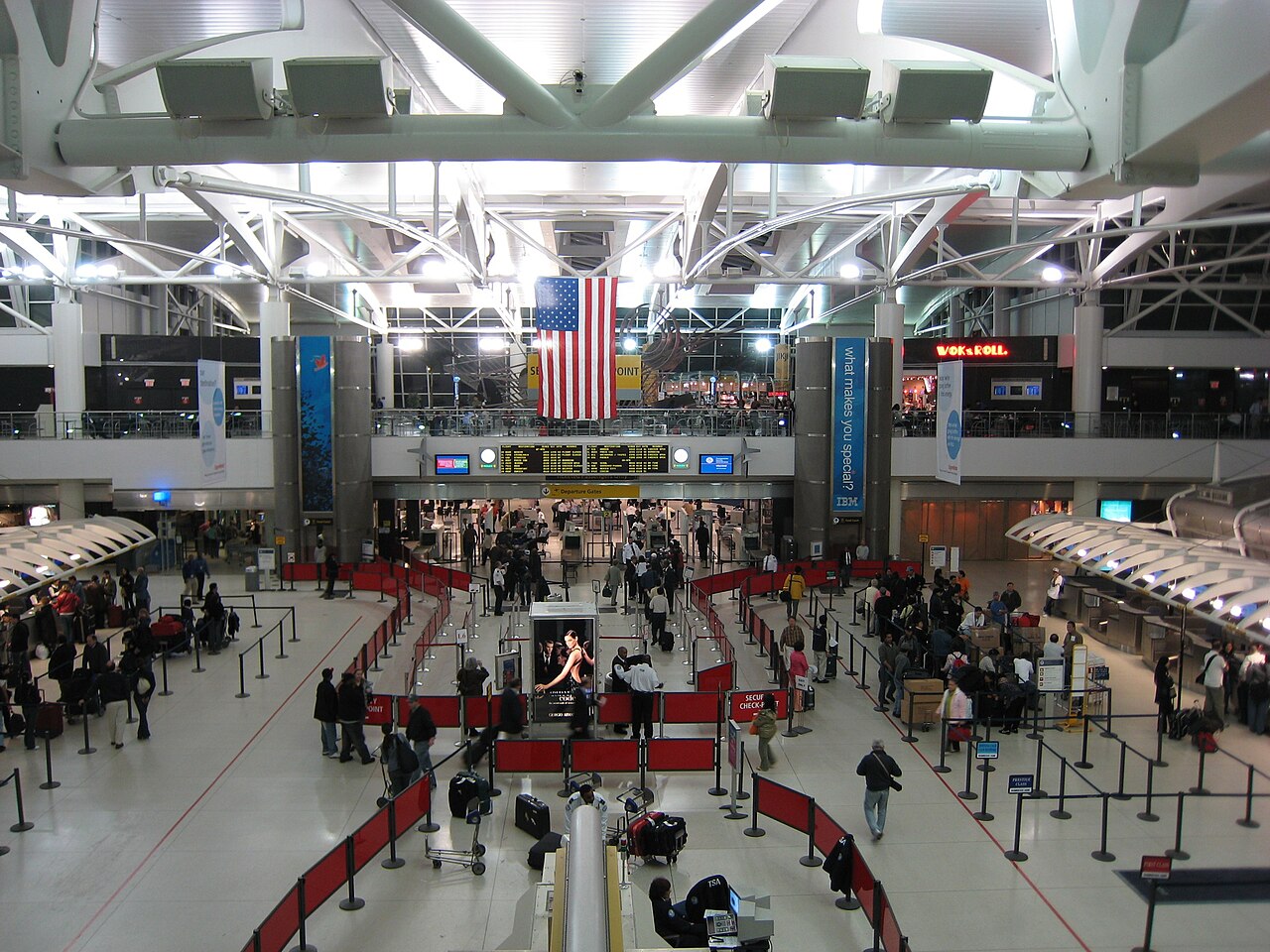 The departures hall of JFK Airport Terminal 1 in New York, with an American flag hanging from the roof above the queue lanes