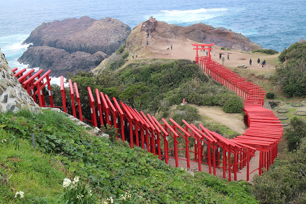 A long line of red torii gates winding down a green clifftop to the sea at Motonosumi Shrine, Nagato, Yamaguchi Prefecture