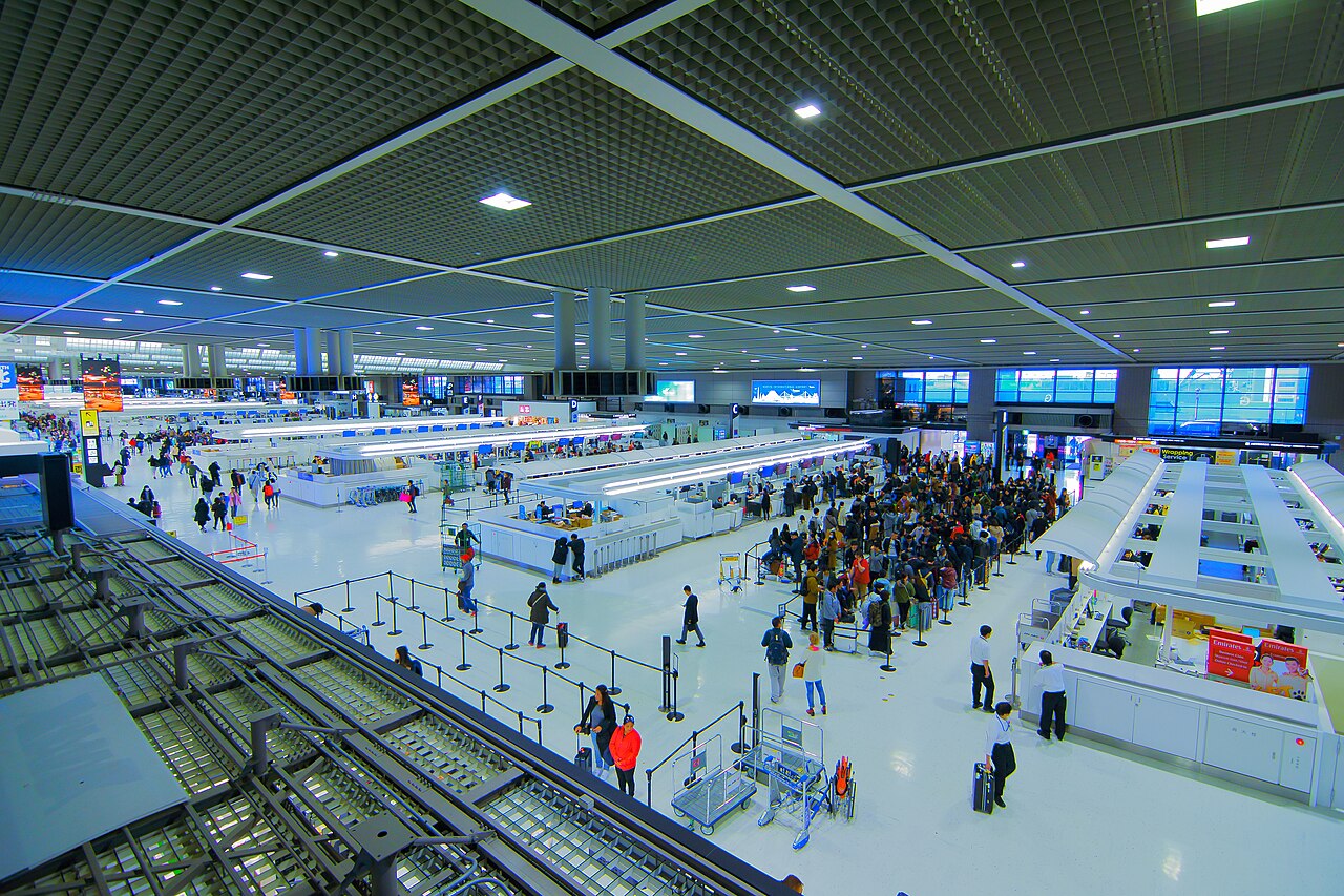 The departure lobby of Narita Airport Terminal 2 seen from above, with rows of check-in counters and travellers queuing