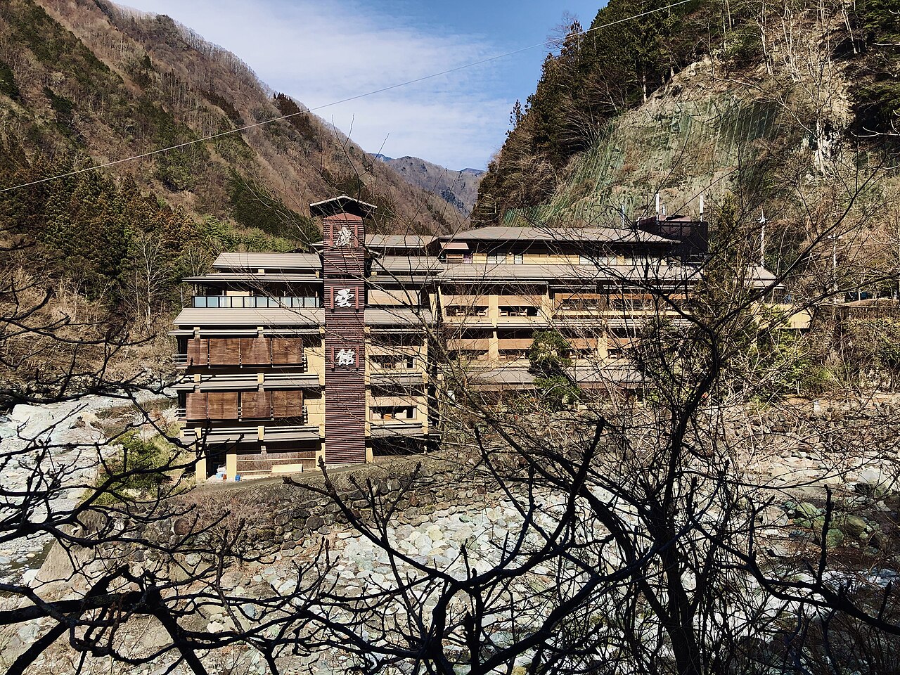 Nishiyama Onsen Keiunkan building with its tall sign tower beside a rocky river in a steep mountain valley in Yamanashi