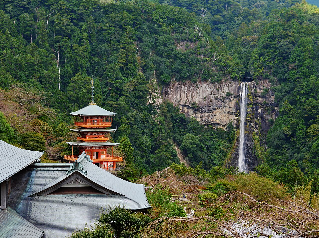 The red three-storey pagoda of Seiganto-ji among forested hills, with Nachi Falls dropping down a cliff behind it