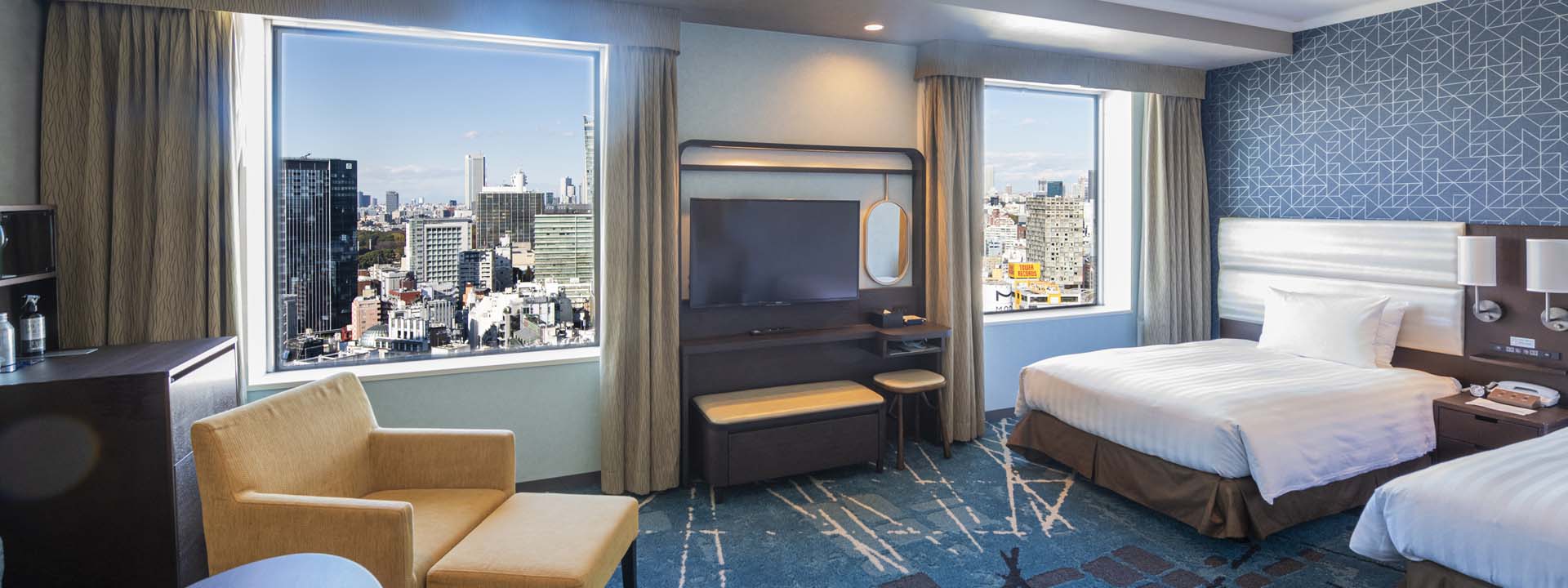 A deluxe twin room at Shibuya Excel Hotel Tokyu, with two beds, an armchair and large windows looking out over the Shibuya skyline