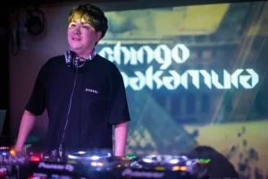 Shingo Nakamura playing a DJ set behind Pioneer decks, with his name projected on the screen behind him