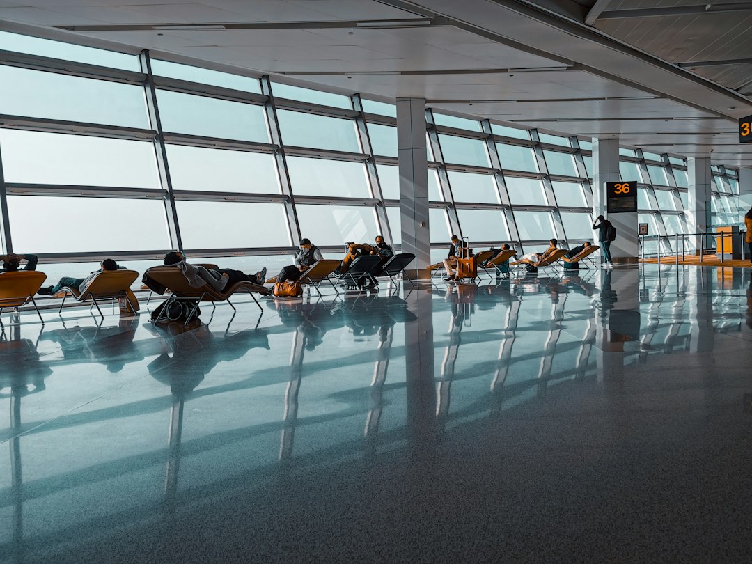 Travellers resting on reclining chairs beside tall windows at an airport departure gate