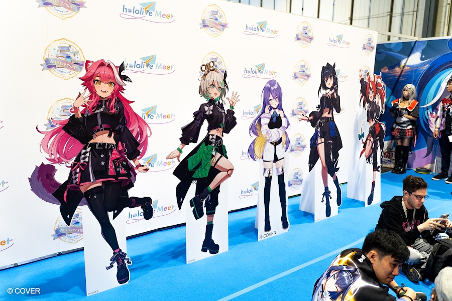 Life size standees of hololive talents in front of a hololive Meet fifth anniversary backdrop at VeXpo 2026