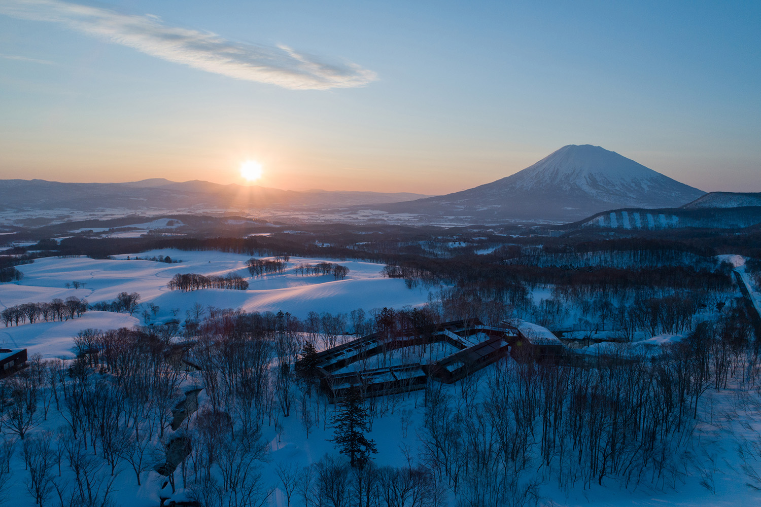 Aerial view of Zaborin in Niseko in winter, surrounded by snowy forest with Mount Yotei behind at sunrise