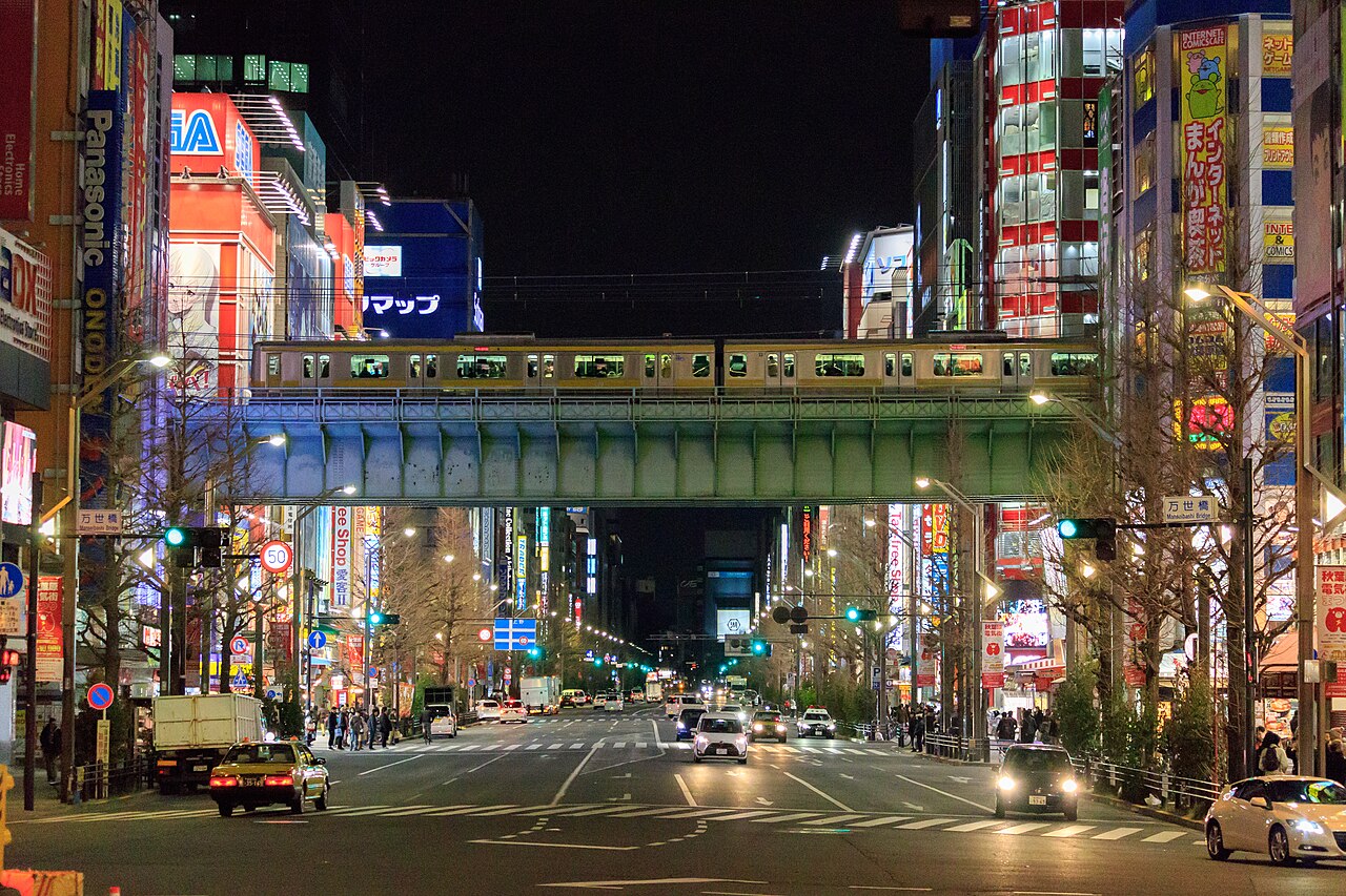 Akihabara’s main street, Chuo Dori, at night with lit shop signs on both sides and a train crossing the railway bridge