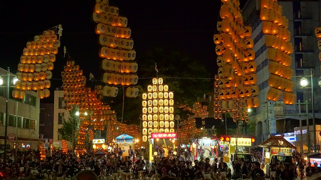 Kanto poles hung with dozens of glowing paper lanterns rising above the crowds at night during the Akita Kanto Festival
