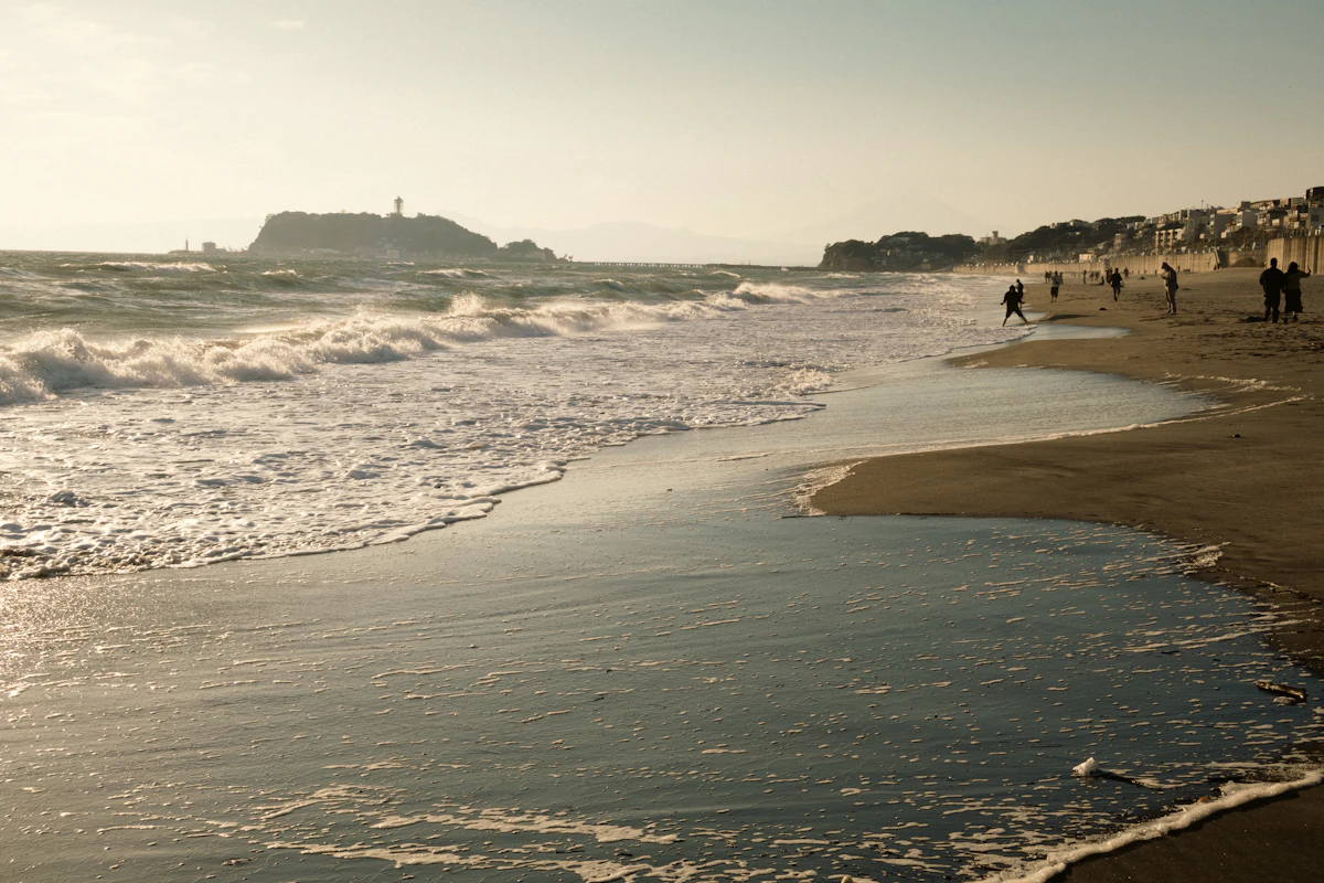 Waves washing onto a sandy beach on the Shōnan coast, with the island of Enoshima on the horizon