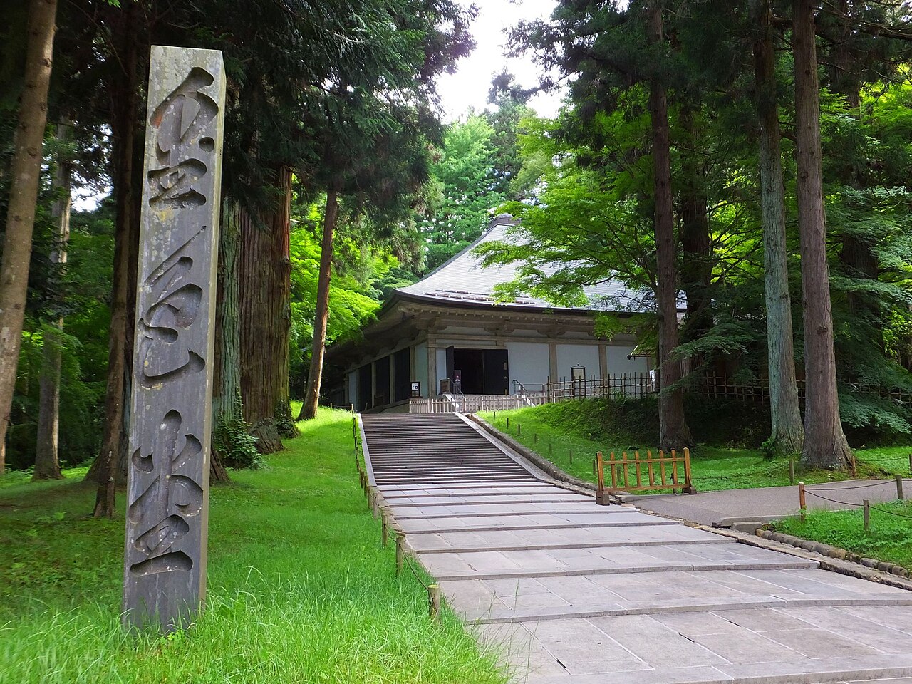 A stone path through tall cedar trees leading to the hall that shelters the Konjikido golden hall at Chuson-ji in Hiraizumi
