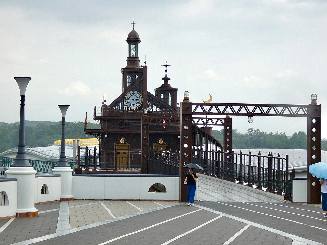 The dark brown Elevator Tower with its clock face and iron bridge on the Hill of Youth at Ghibli Park