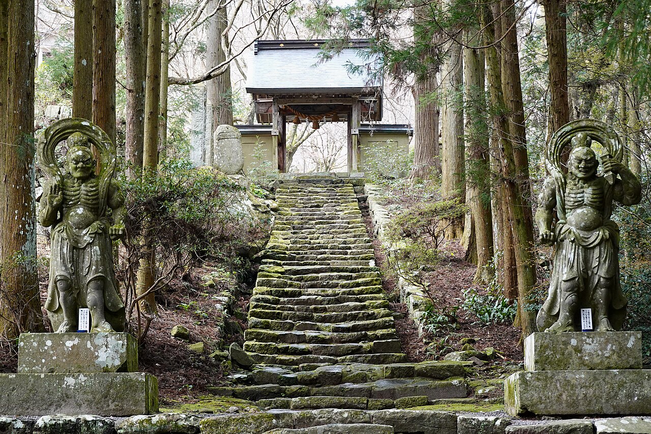 Two moss covered stone Nio guardian statues flanking the stone stairway up to Futago-ji temple in the cedar forest of the Kunisaki Peninsula, Oita