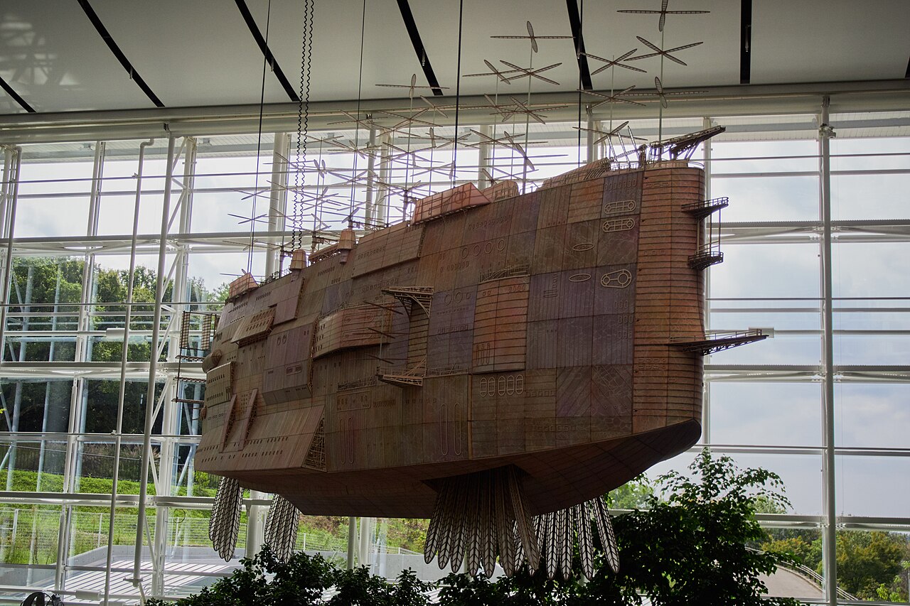 A large wooden airship model with propellers hanging beneath the glass skylight inside Ghibli’s Grand Warehouse