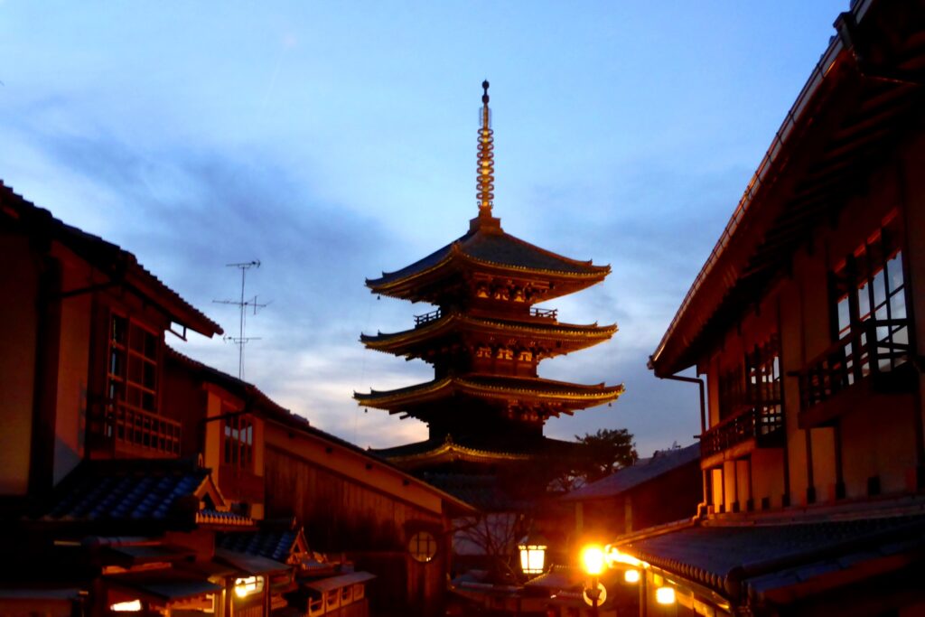 The five storey Yasaka Pagoda of Hokan-ji at dusk, framed by old wooden houses and lit lanterns in Higashiyama, Kyoto