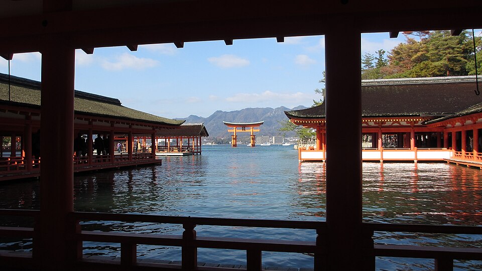 View from a vermilion corridor of Itsukushima Shrine on Miyajima at high tide, with the great torii gate standing in the sea