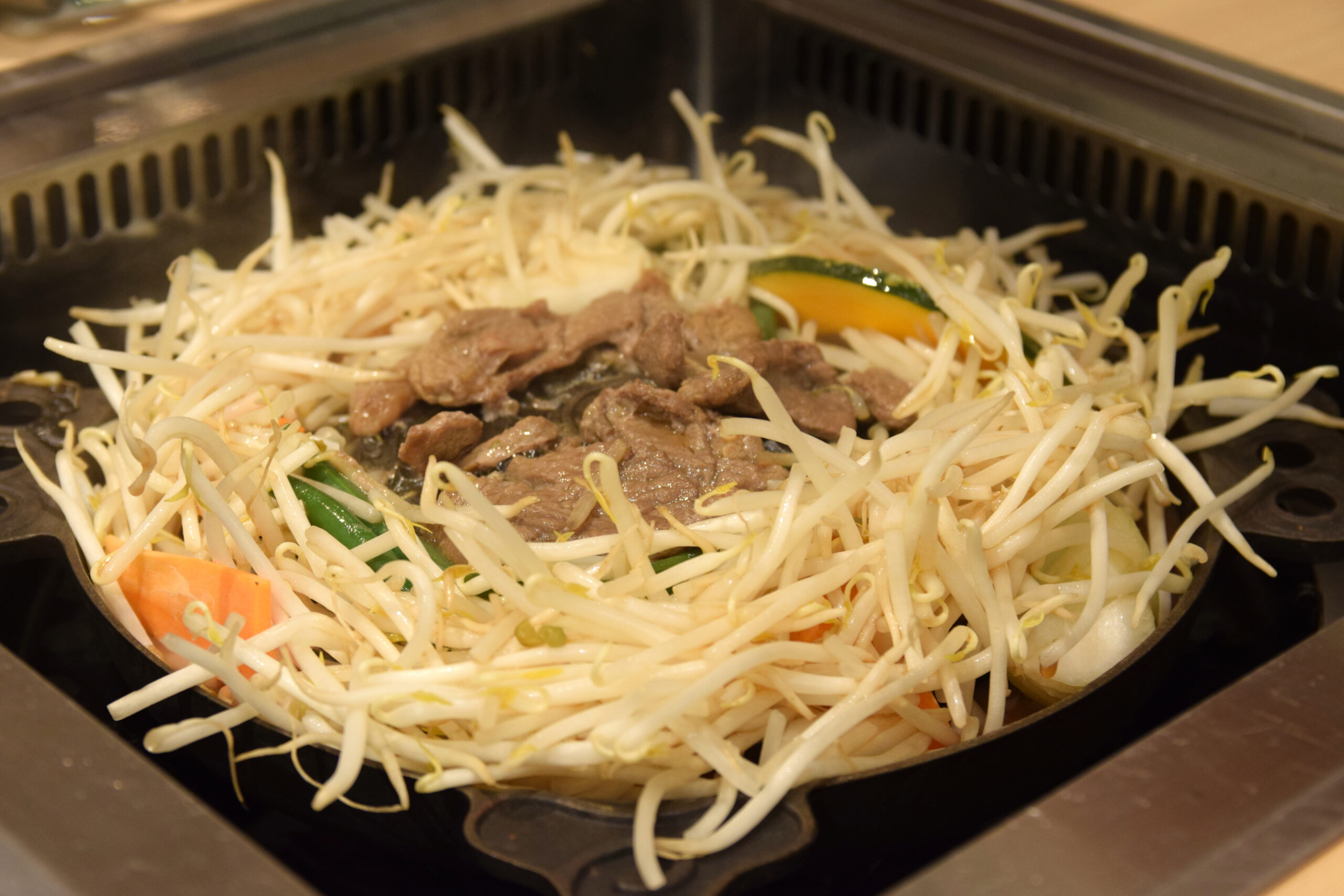 Slices of lamb grilling in the middle of a jingisukan pan, surrounded by a pile of bean sprouts and vegetables