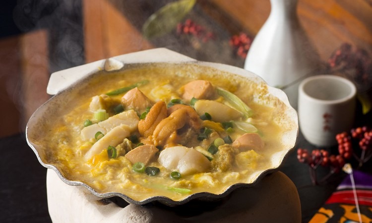 Kaiyaki miso bubbling in a large scallop shell, with scallops, sea urchin and spring onion set in miso and egg