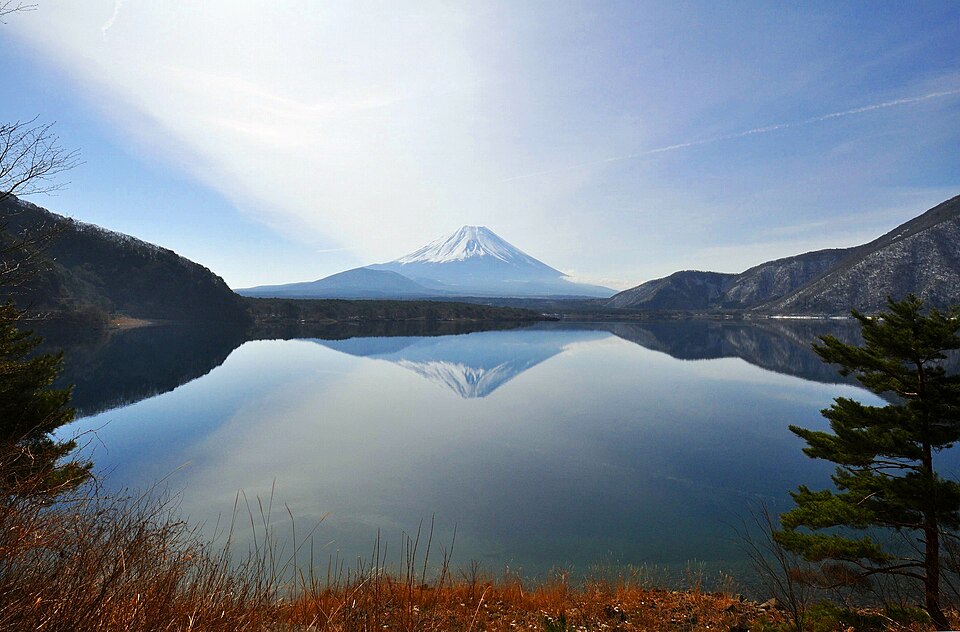 Mount Fuji reflected in the still water of Lake Motosu between wooded hills