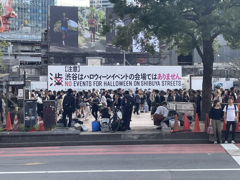 Shibuya ward banner by the station reading No Events for Halloween on Shibuya Streets, with a crowd waiting below