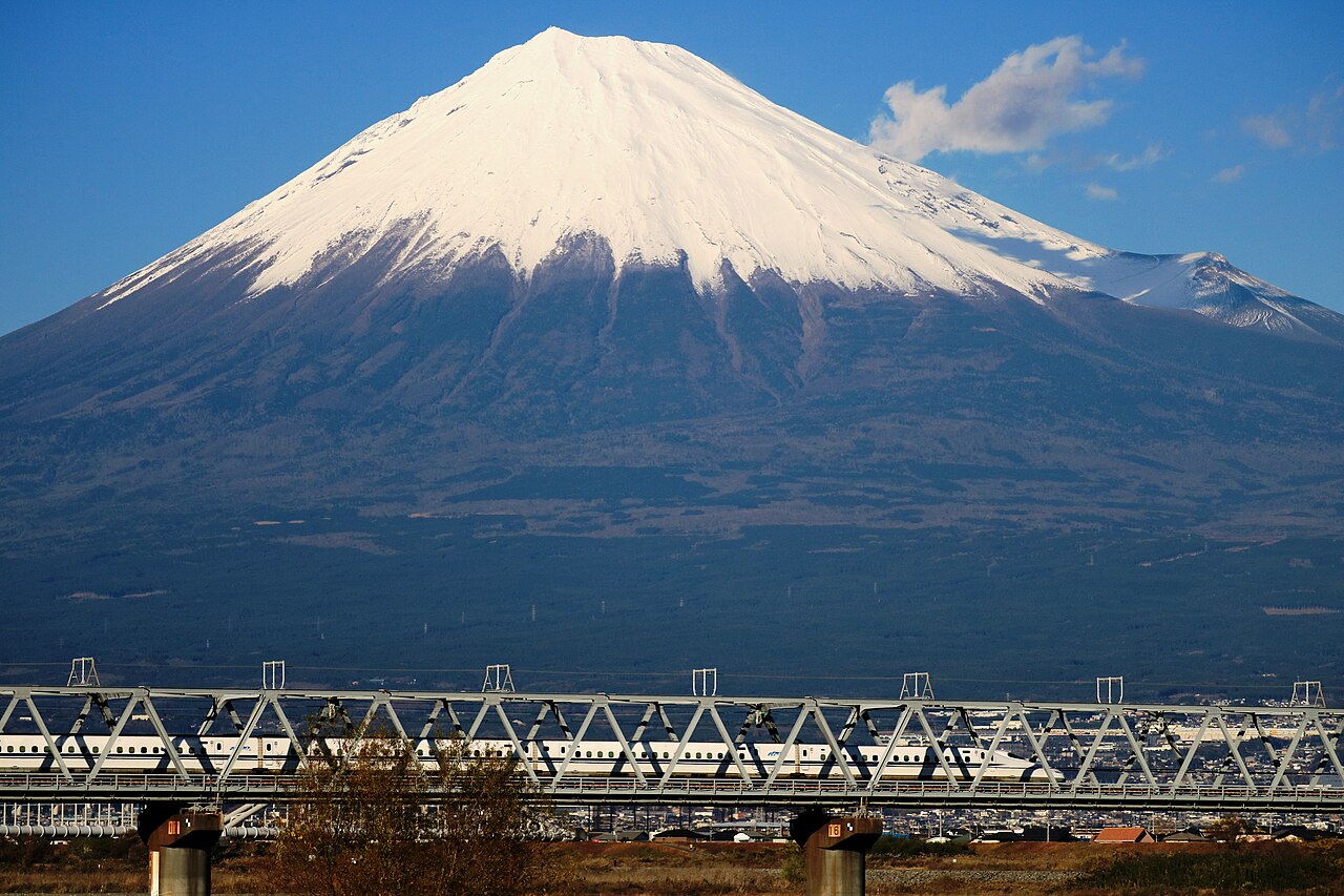 Shinkansen N700 train crossing a bridge below snow-capped Mount Fuji