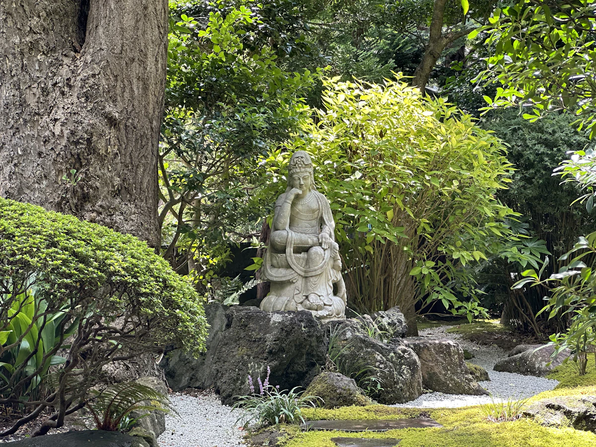 A stone Buddhist statue among rocks, raked gravel and greenery in the garden at Hōkoku-ji, Kamakura