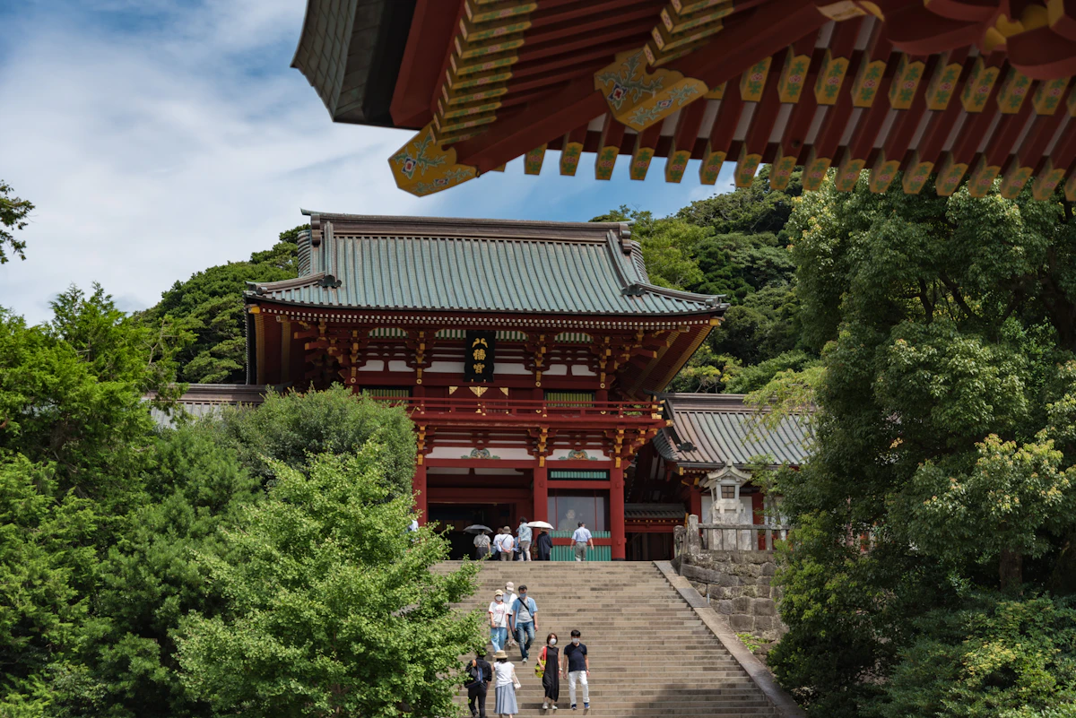 The red main hall of Tsurugaoka Hachimangu at the top of its stone staircase, with visitors climbing the steps