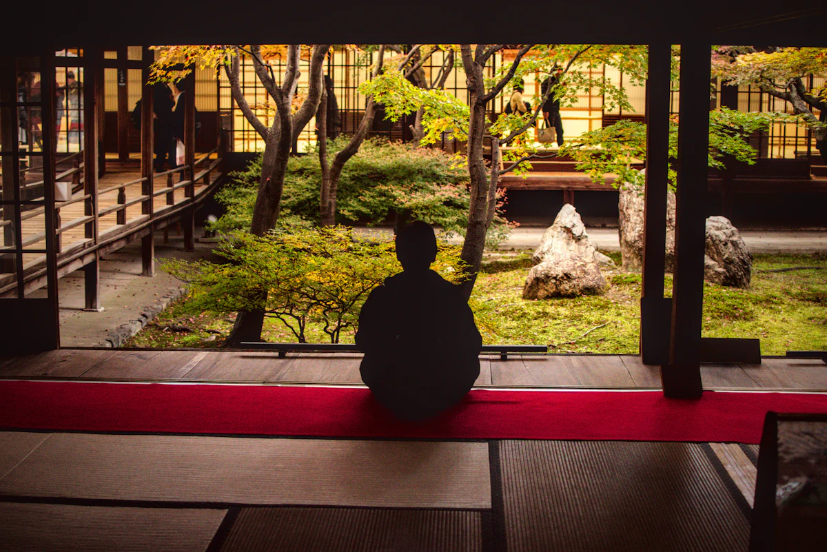 A visitor sits quietly on a temple veranda facing a moss and stone Zen garden