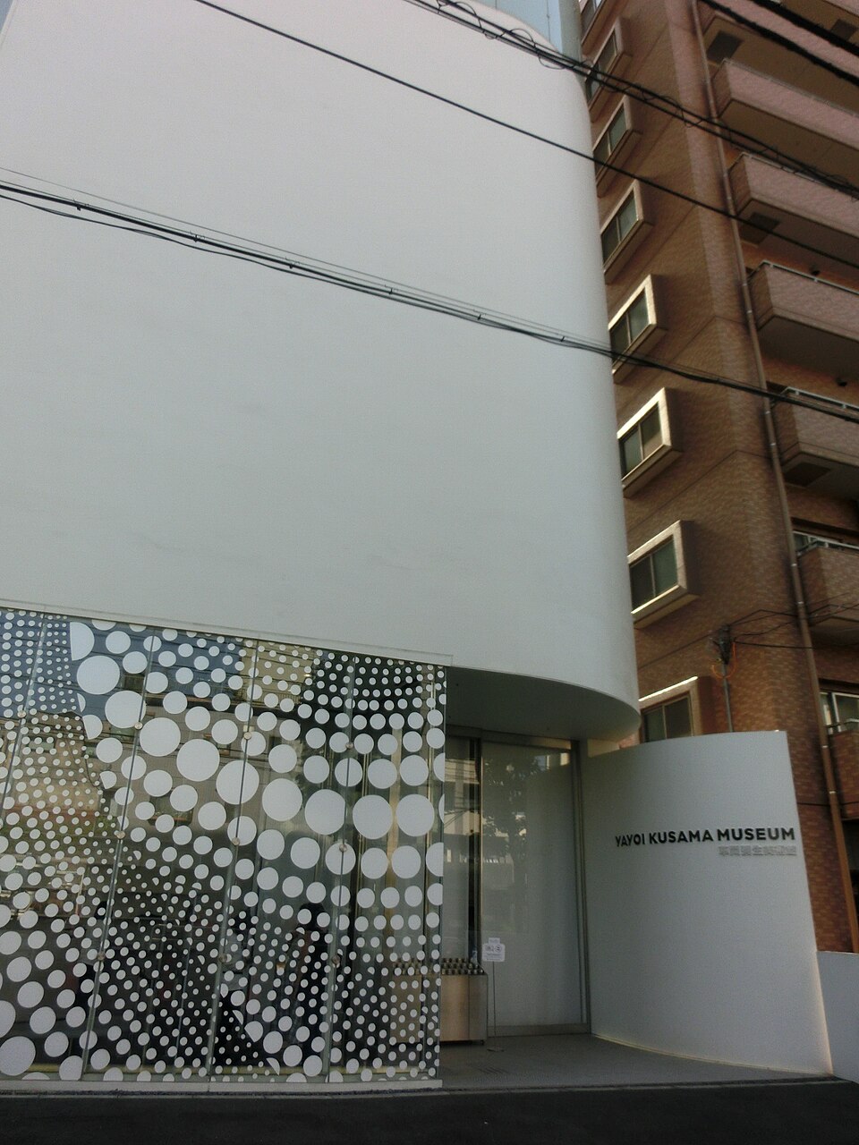 The white curved front of the Yayoi Kusama Museum in Shinjuku, with polka dot glass panels around the entrance