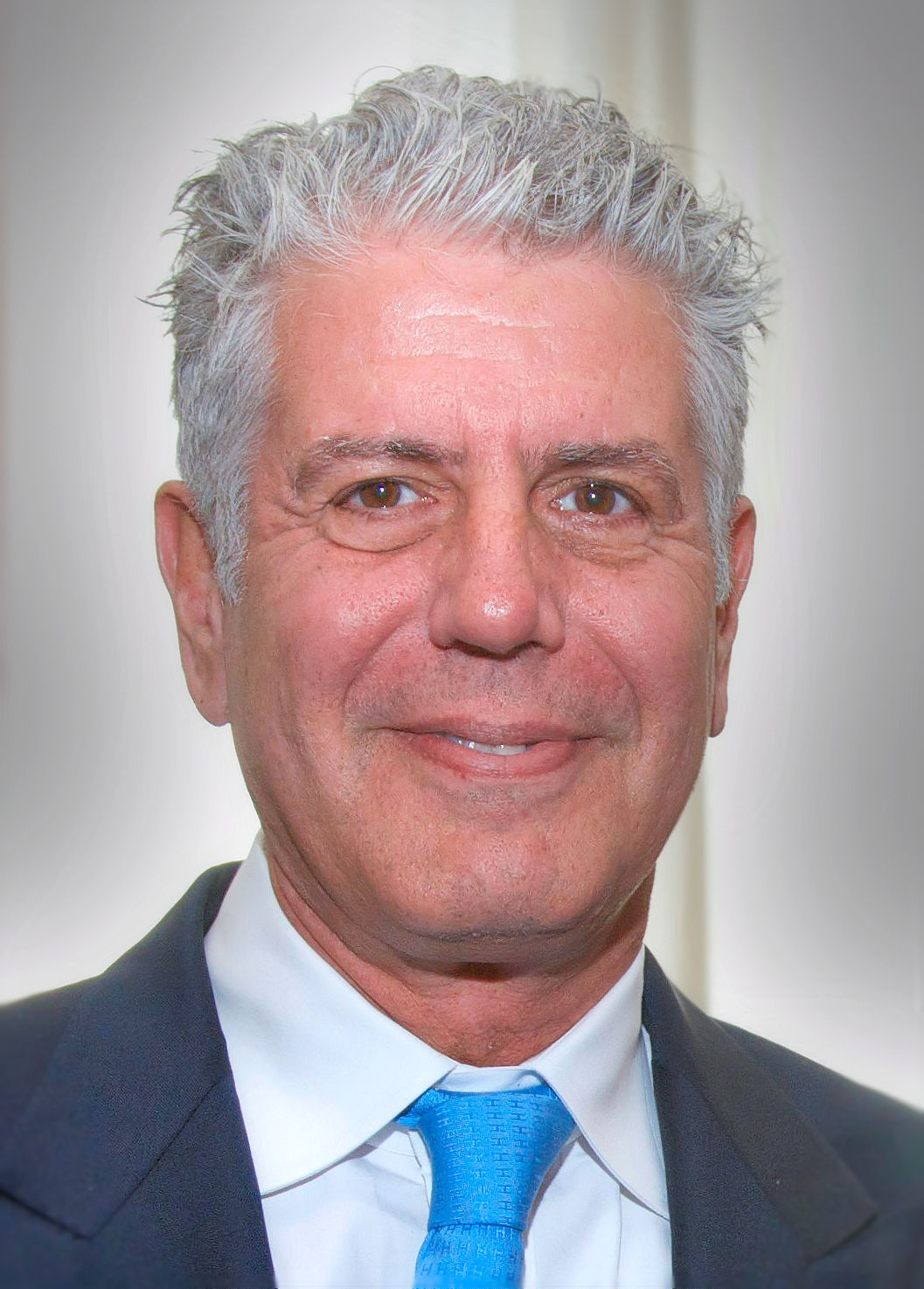 Anthony Bourdain smiling in a suit and blue tie at the Peabody Awards in 2014