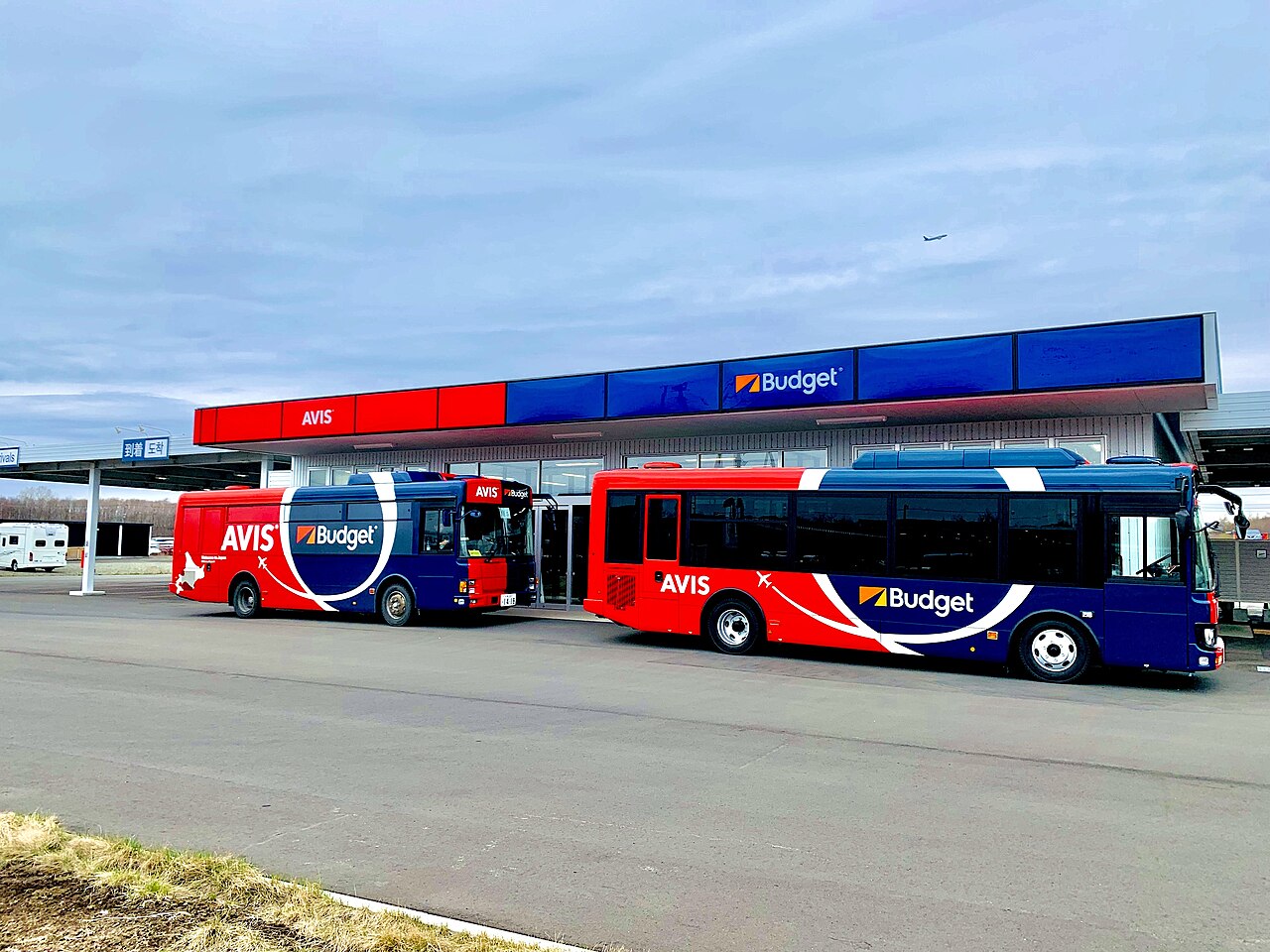 Avis and Budget rental car office near New Chitose Airport with two red and blue shuttle buses parked outside